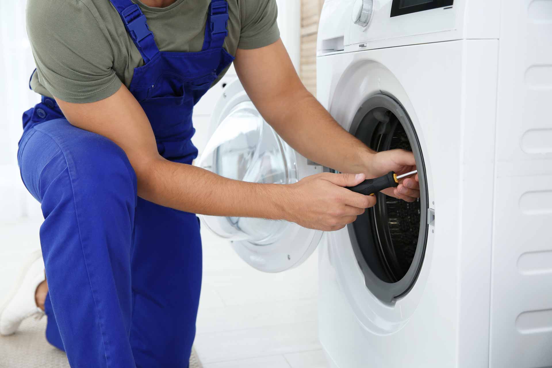 A technician in blue overalls repairs a dryer