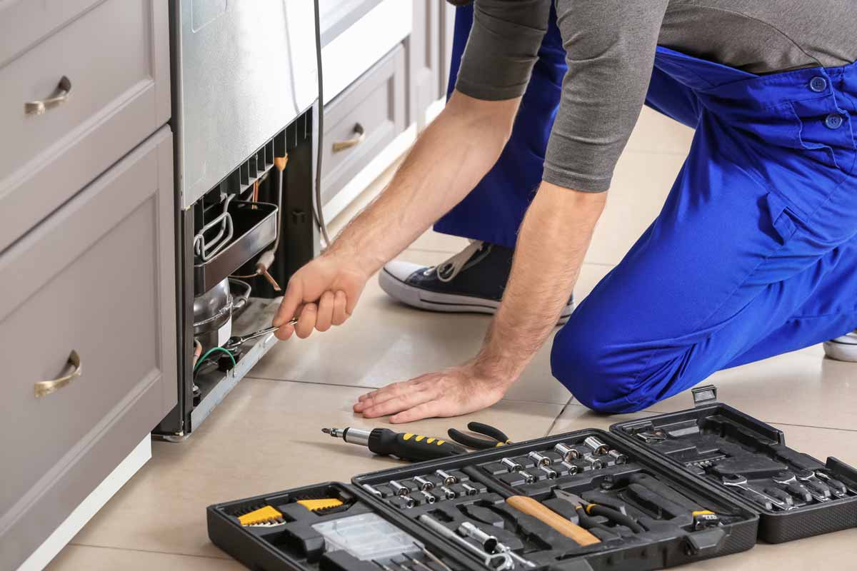 Technician kneeling to repair a refrigerator