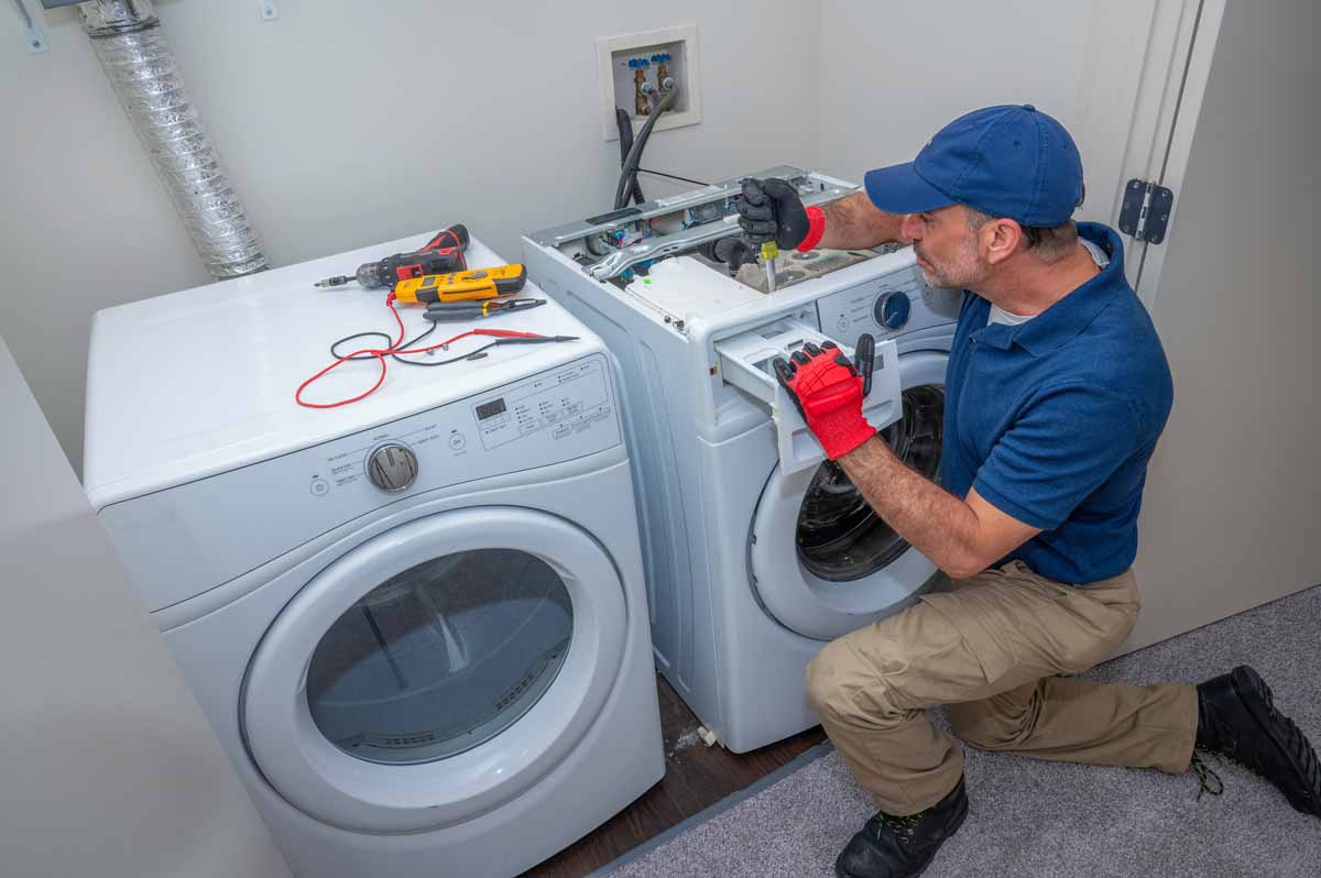 A technician in a blue uniform repairs a washing machine
